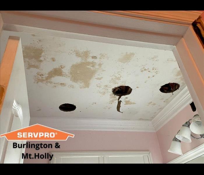White bathroom ceiling with three holes and brown discoloration.