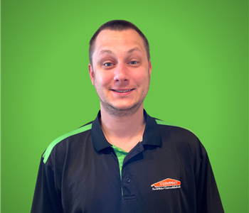 A male servpro employee smiles infront of a green background.