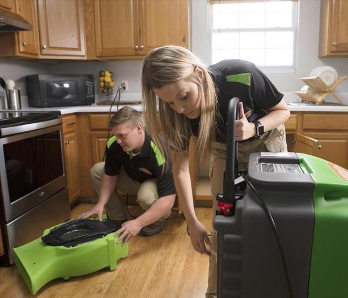 Two SERVPRO technicians setting up equipment in a kitchen.